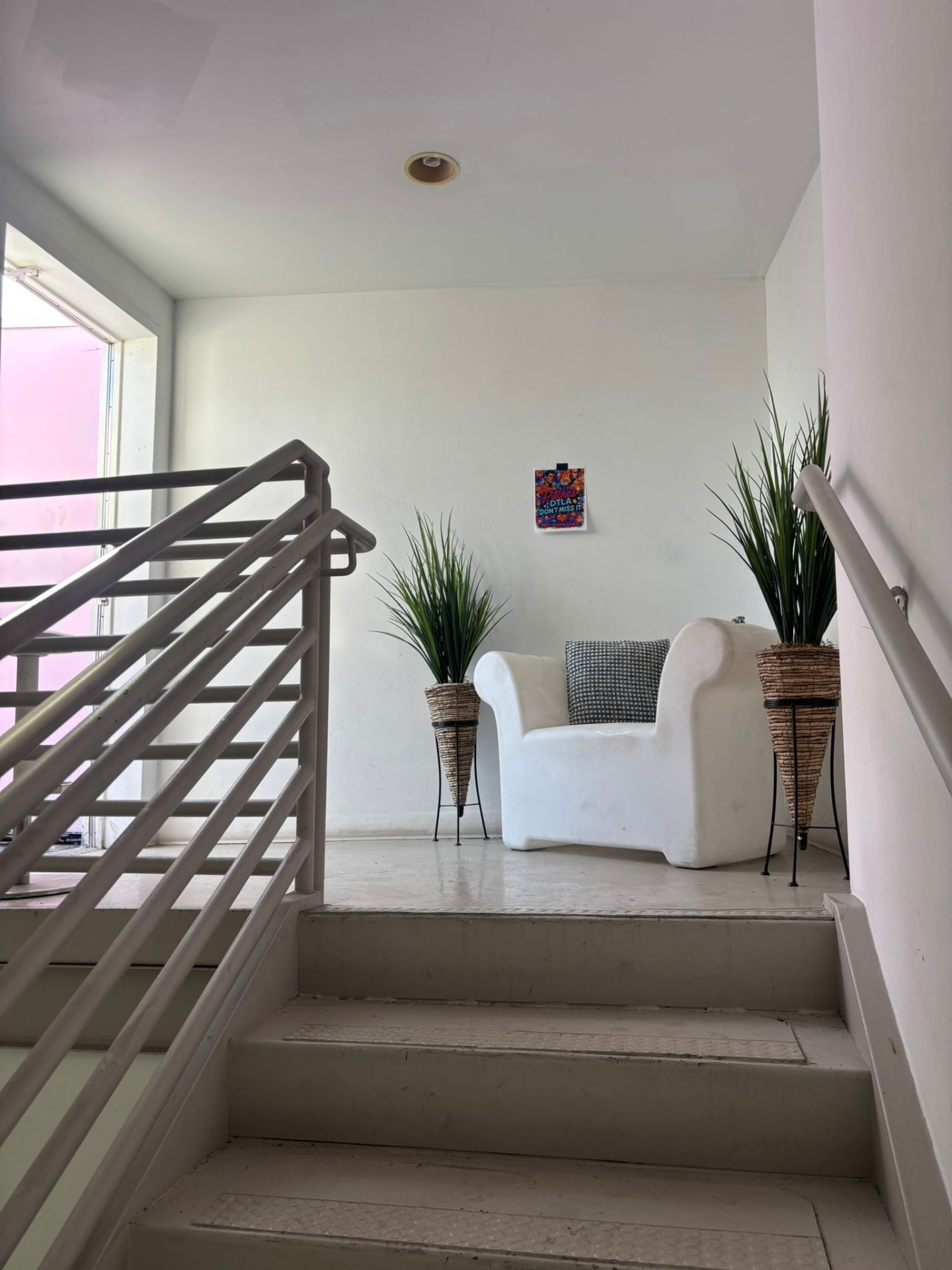 Stair landing with a sculptural white armchair and potted grasses