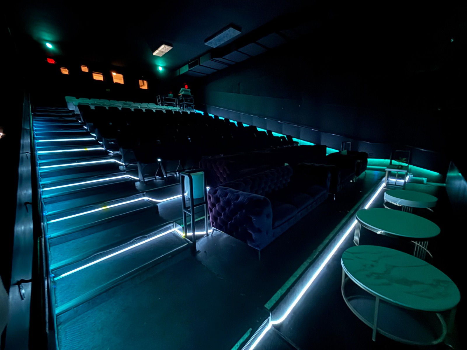 Theater house with teal LED aisle lighting and marble cocktail tables