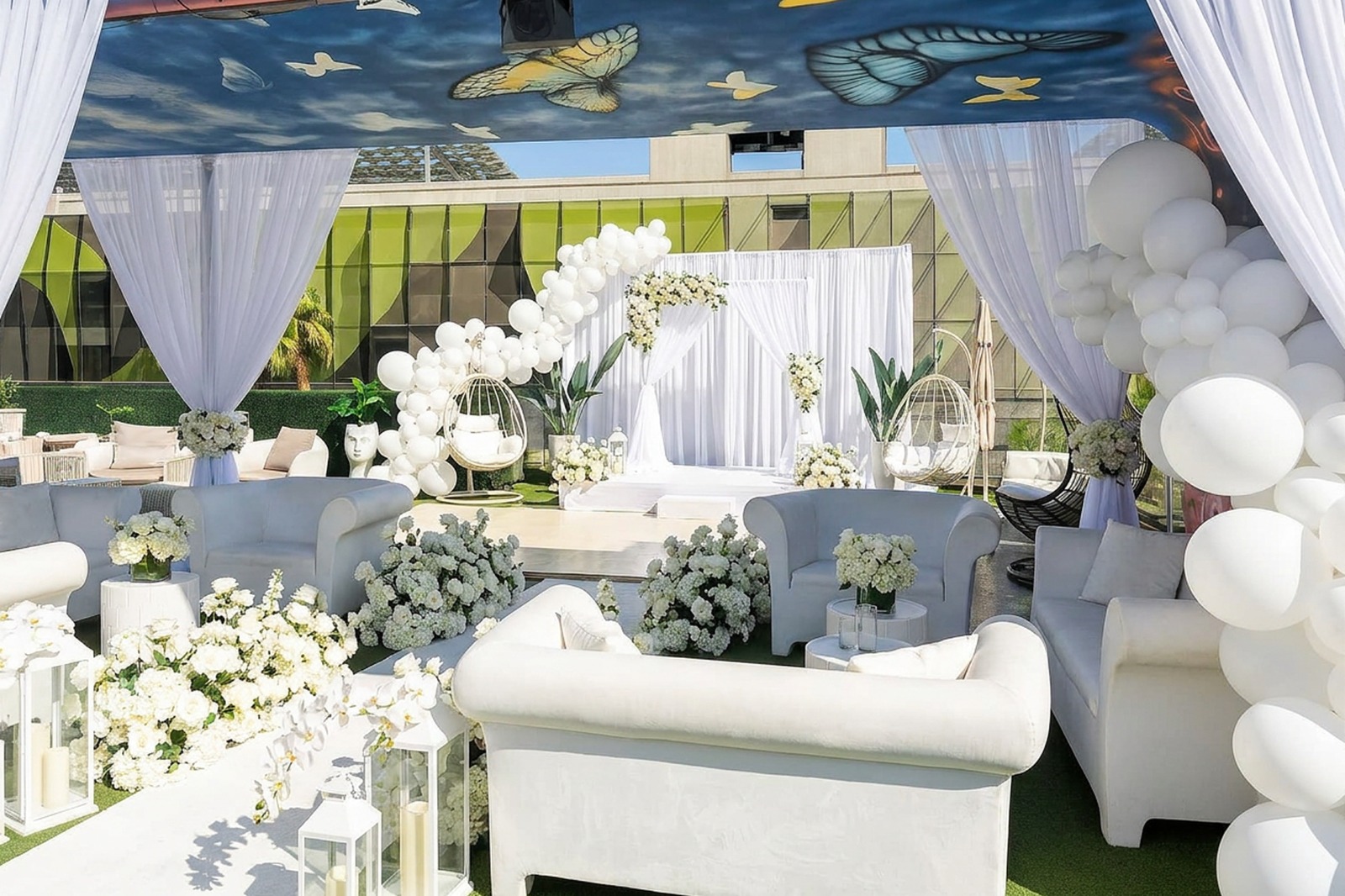 All-white rooftop ceremony setup with floral arch, drapery and lounge seating under the butterfly ceiling