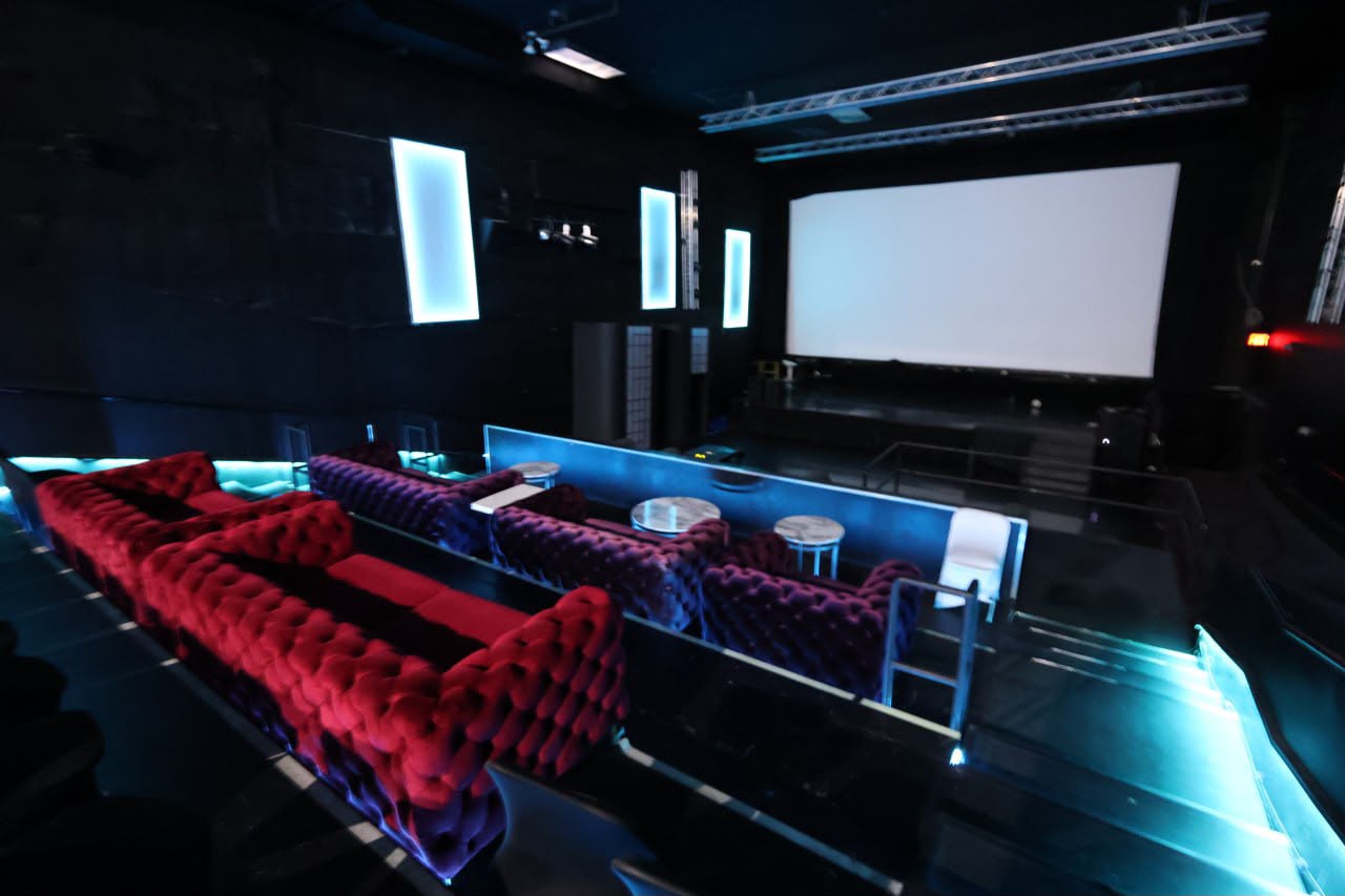 The theater screen beyond velvet sofa rows and blue LED aisles