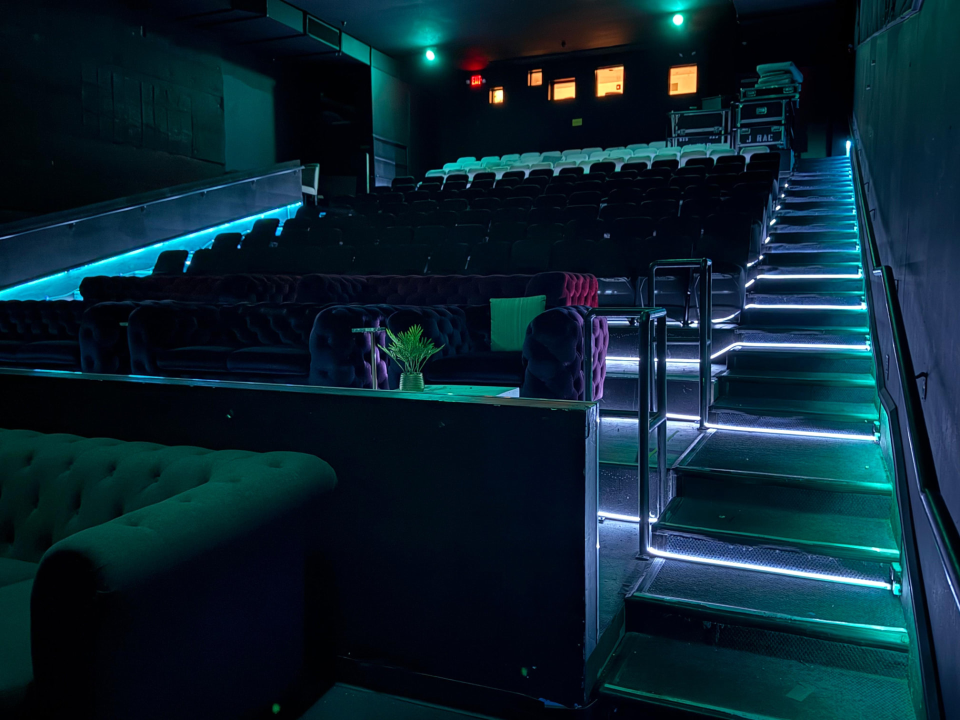 Tiered theater seating with tufted velvet sofas under teal light