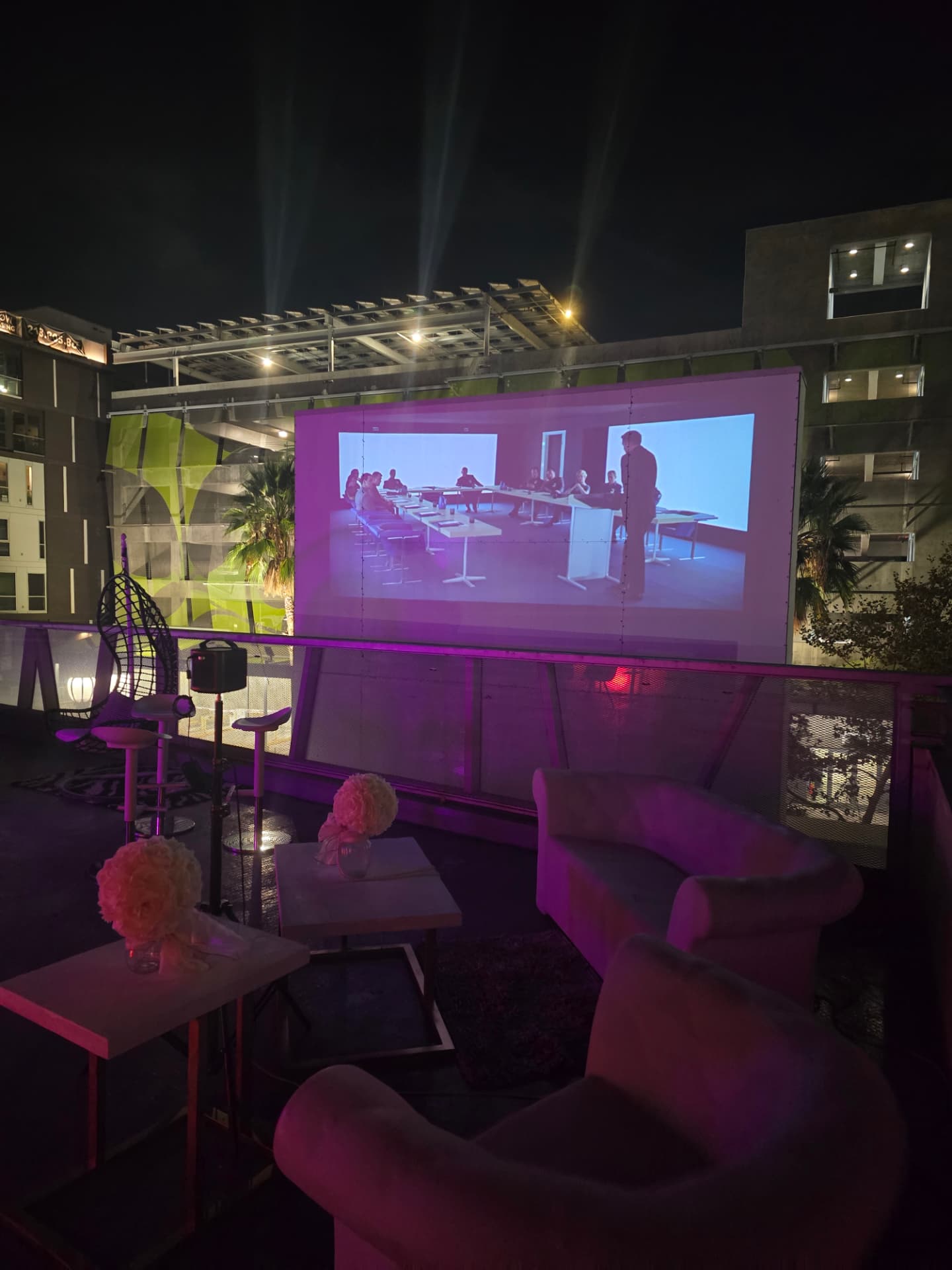 A rooftop screening setup with a large screen and pink-lit sofas