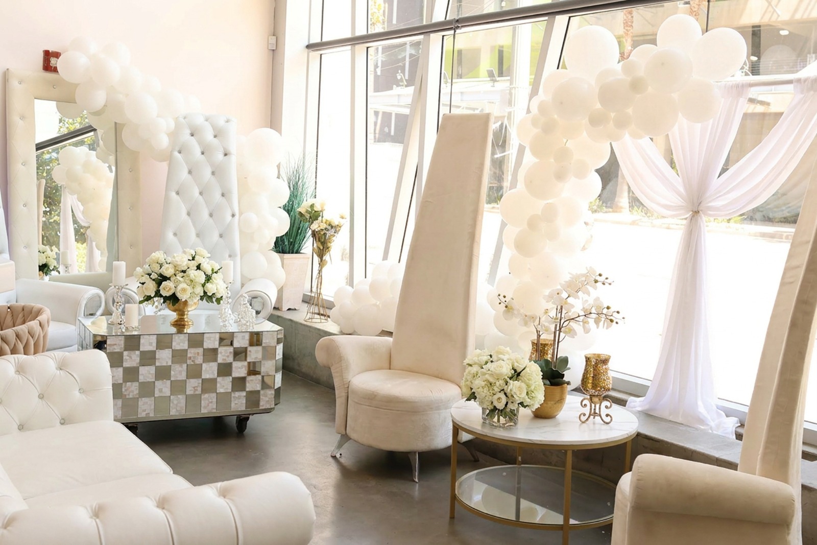 Sunlit lobby lounge with white balloon garlands, drapery and tufted throne seating