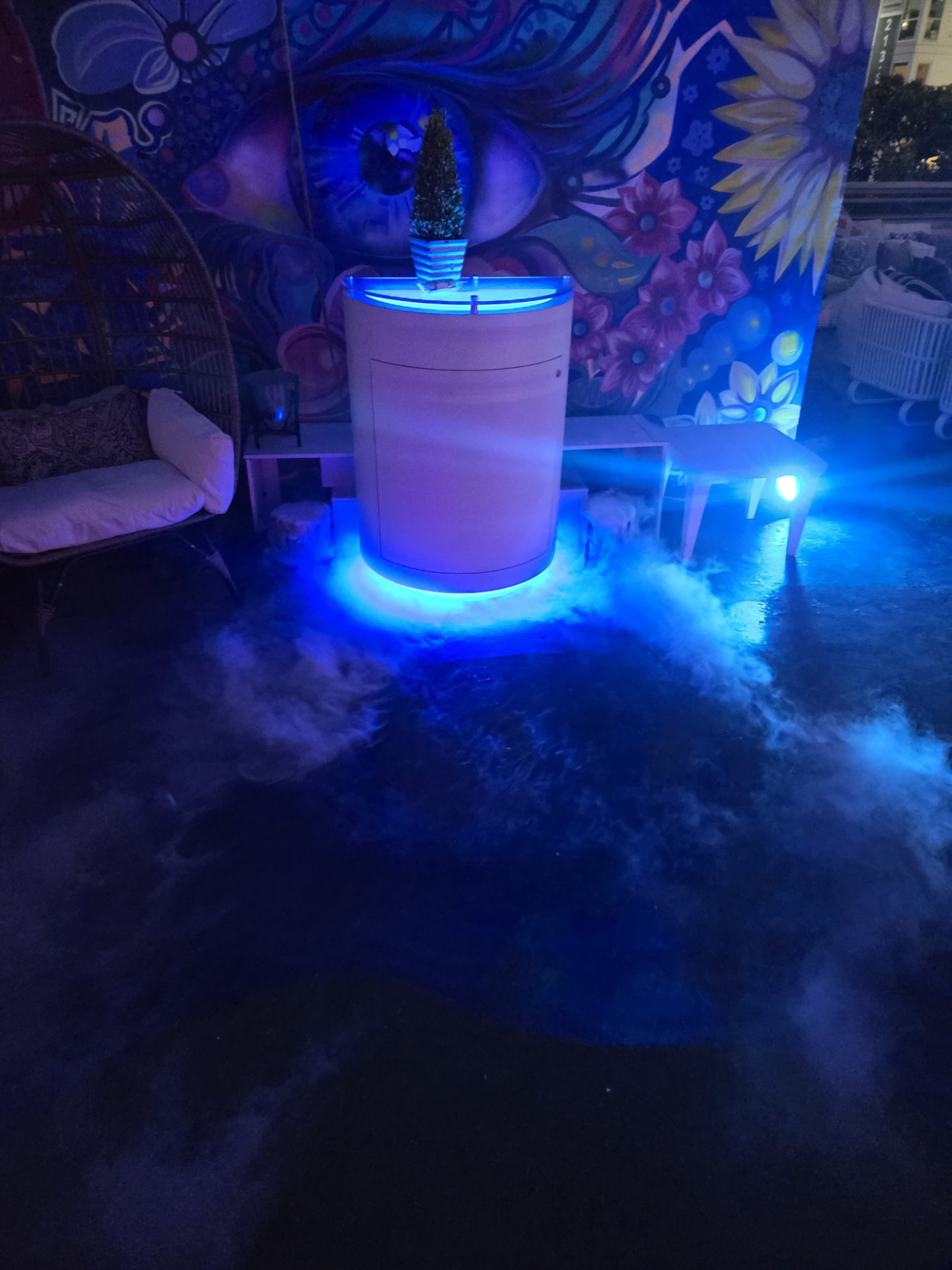 Rooftop bar lit blue with low fog against the mural wall at night