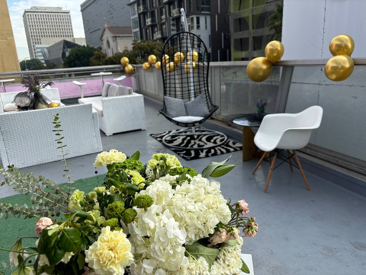Rooftop lounge dressed with white florals, gold balloons and a hanging swing chair