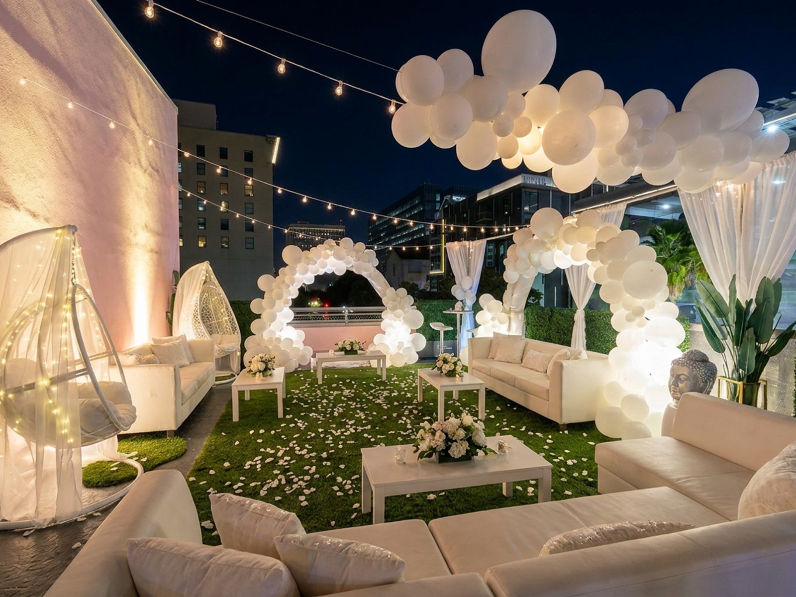 All-white rooftop ceremony at night with balloon arches, string lights and petal-strewn lawn