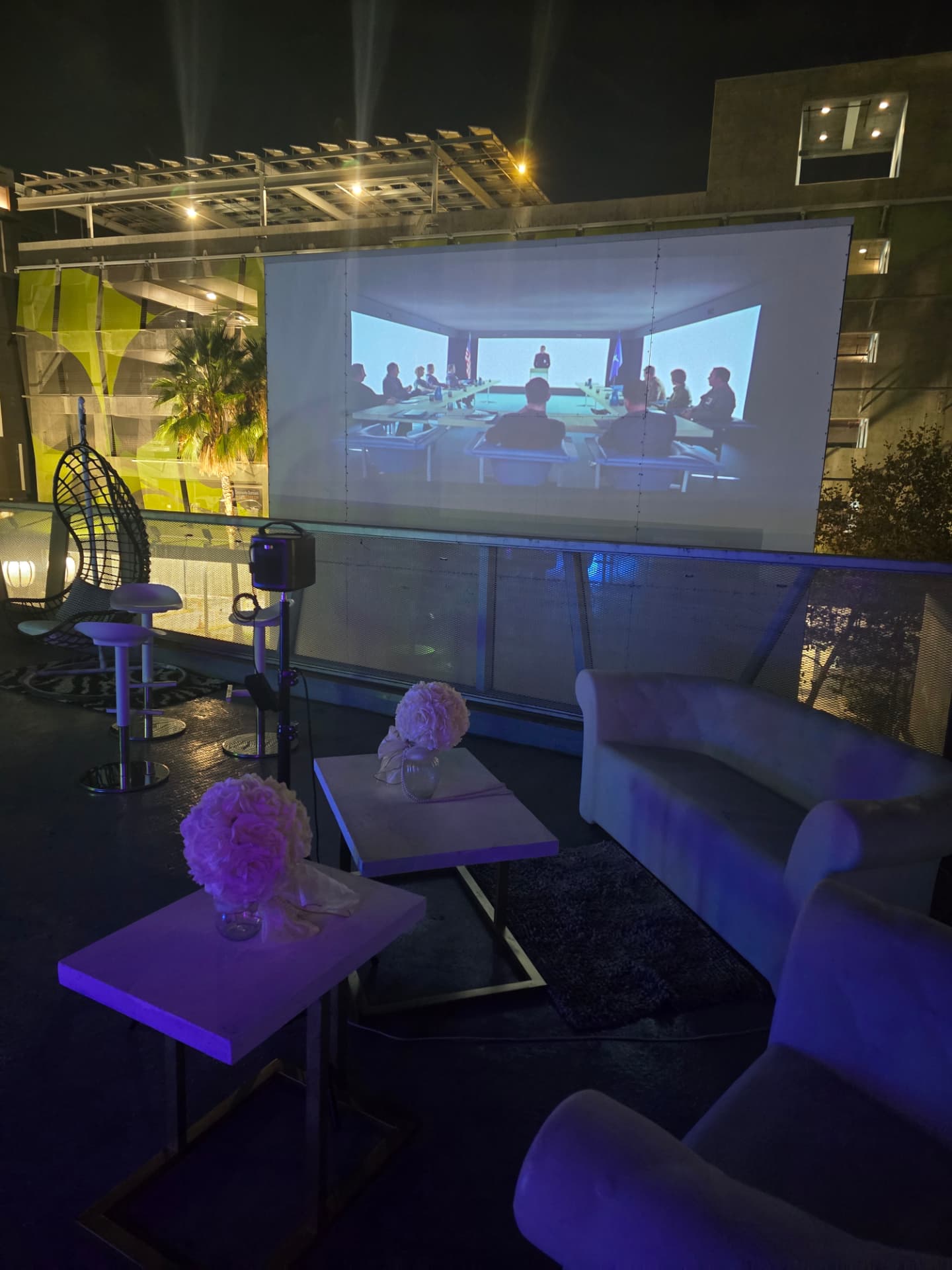 A rooftop screening at night with white sofas under purple light